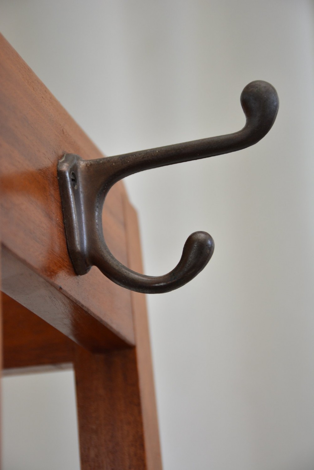A tall, square-framed Art Deco wooden coat stand with dark metal hanging hooks and a lower umbrella drip tray. View XI