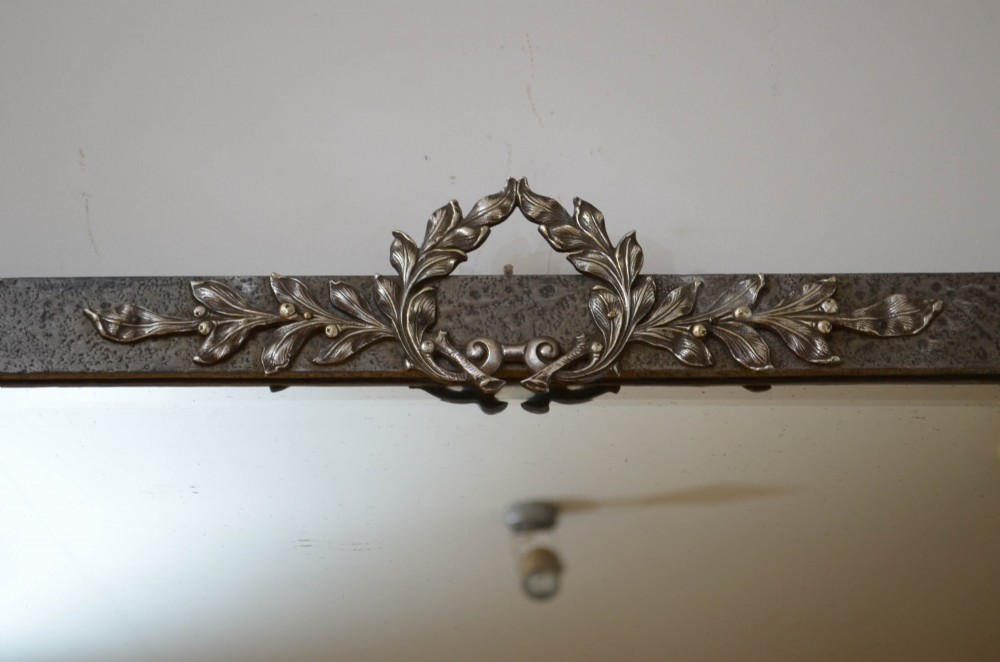 A rectangular Arts and Crafts wall mirror with a hand-hammered silver metal frame, decorated with fleur-de-lis corner accents and a foliate wreath crest. View V