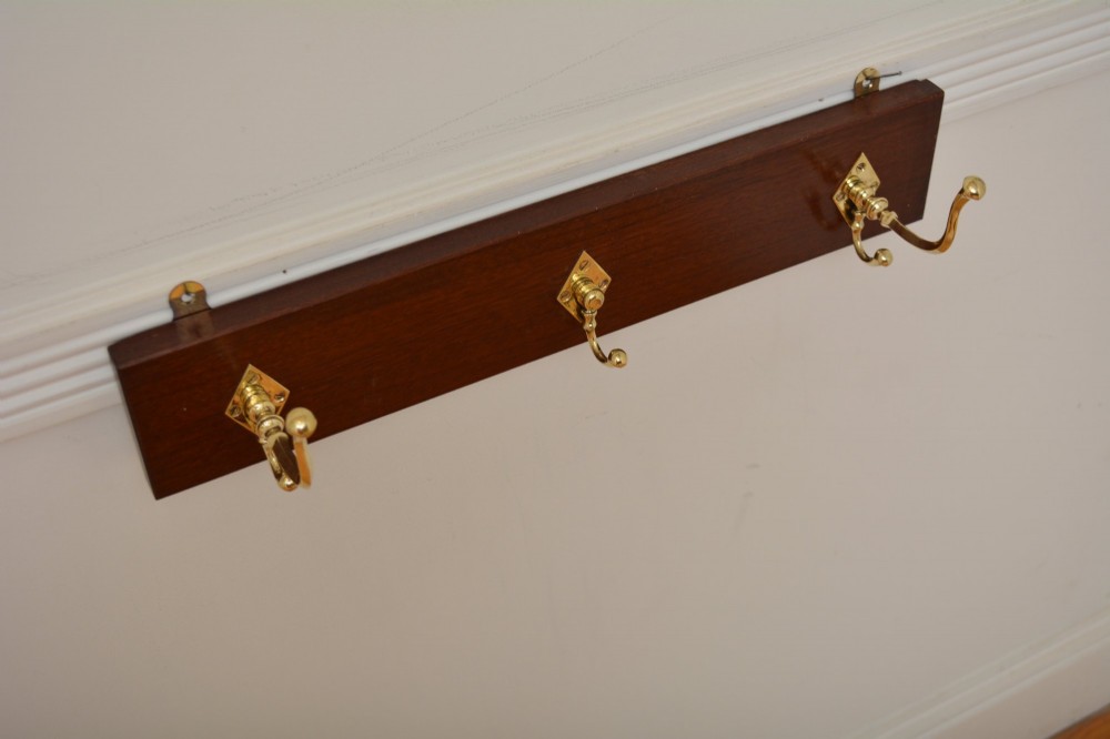 A rectangular polished mahogany backboard mounted with three polished brass double coat hooks featuring diamond-shaped backplates. View II