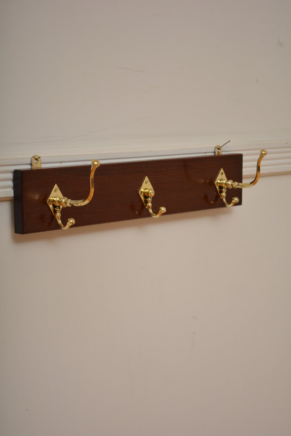 A rectangular polished mahogany backboard mounted with three polished brass double coat hooks featuring diamond-shaped backplates. View IV