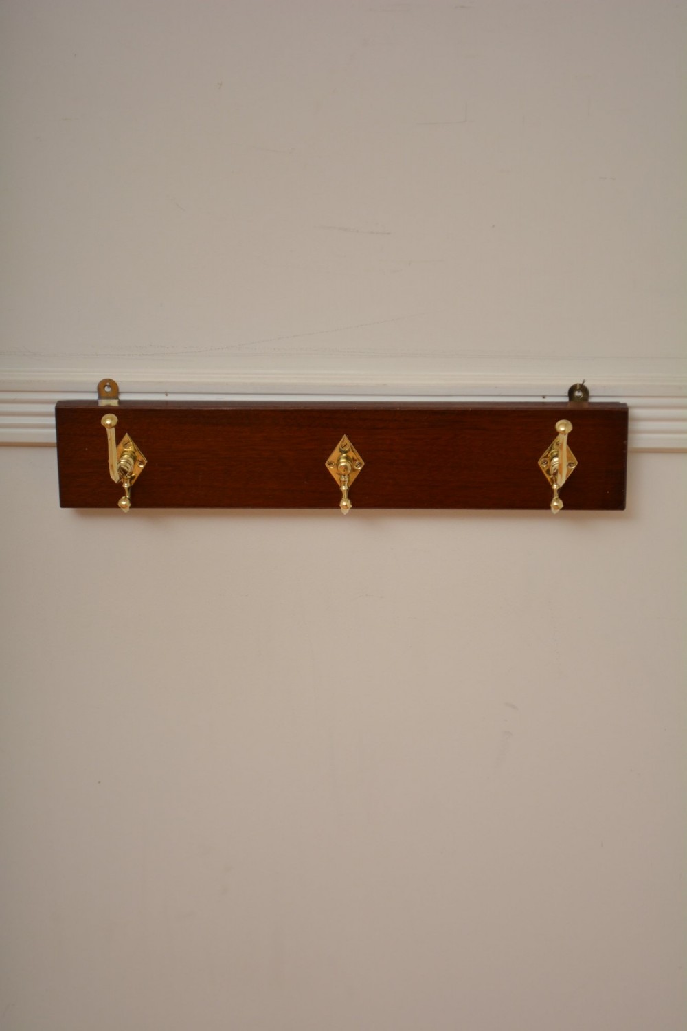 A rectangular polished mahogany backboard mounted with three polished brass double coat hooks featuring diamond-shaped backplates. View V