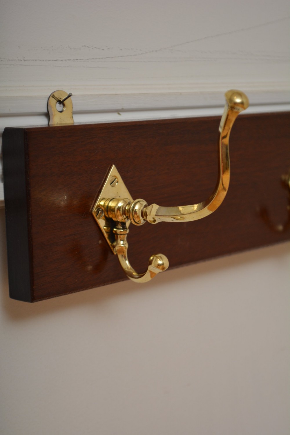 A rectangular polished mahogany backboard mounted with three polished brass double coat hooks featuring diamond-shaped backplates. View VI
