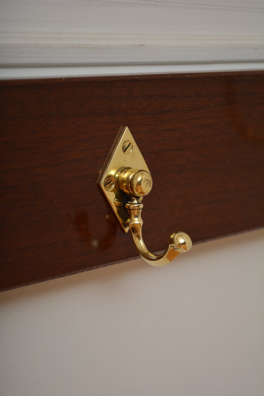 A rectangular polished mahogany backboard mounted with three polished brass double coat hooks featuring diamond-shaped backplates. View VII