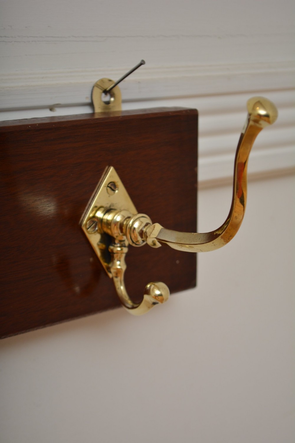 A rectangular polished mahogany backboard mounted with three polished brass double coat hooks featuring diamond-shaped backplates. View VIII