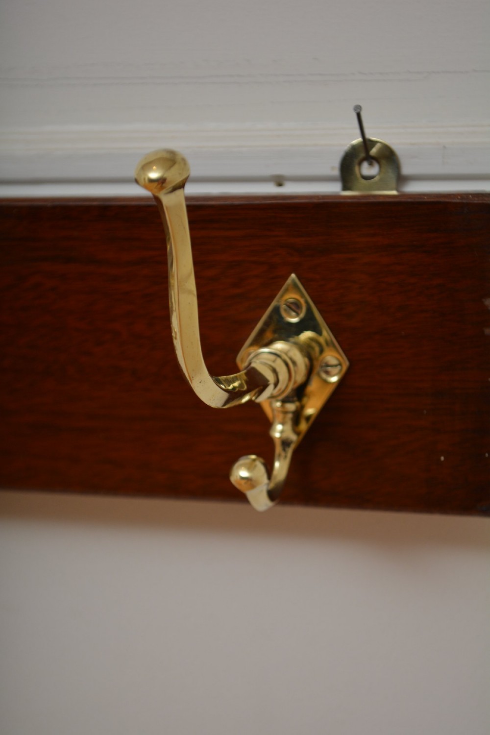 A rectangular polished mahogany backboard mounted with three polished brass double coat hooks featuring diamond-shaped backplates. View IX