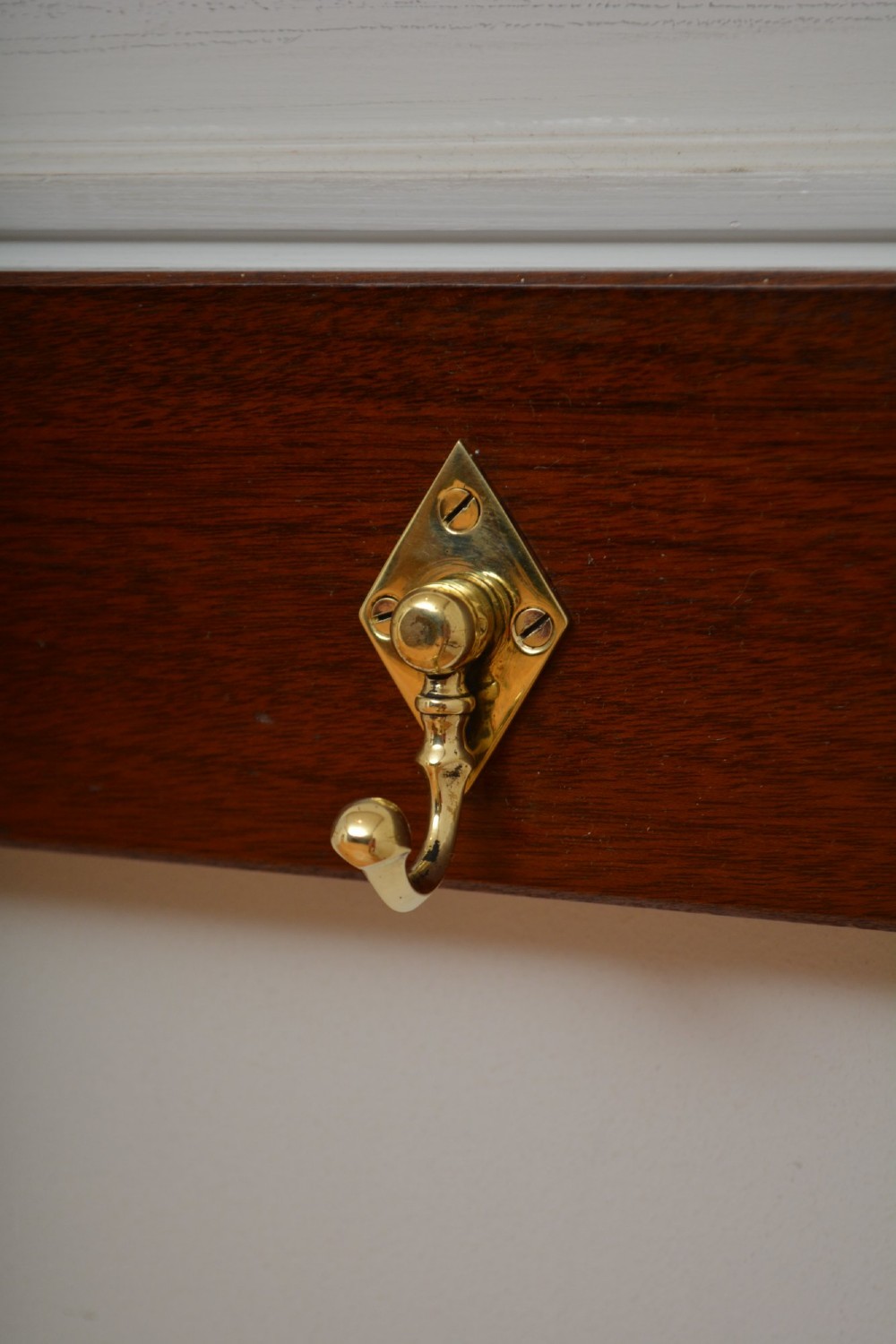 A rectangular polished mahogany backboard mounted with three polished brass double coat hooks featuring diamond-shaped backplates. View X