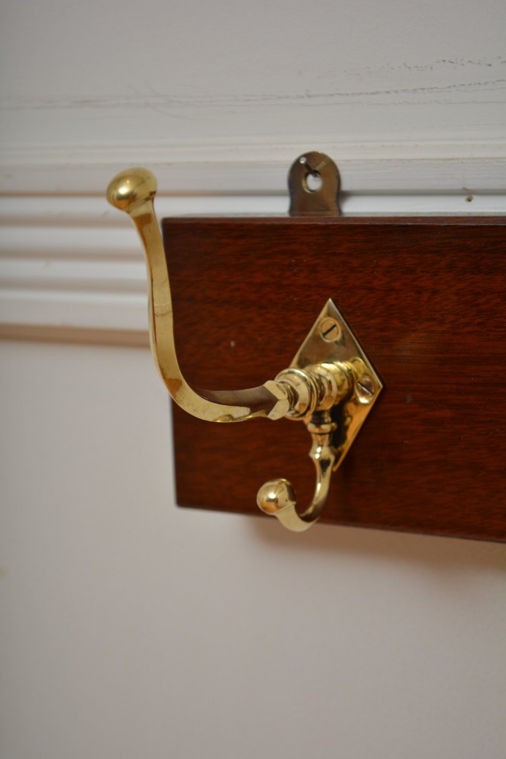 A rectangular polished mahogany backboard mounted with three polished brass double coat hooks featuring diamond-shaped backplates. View XI
