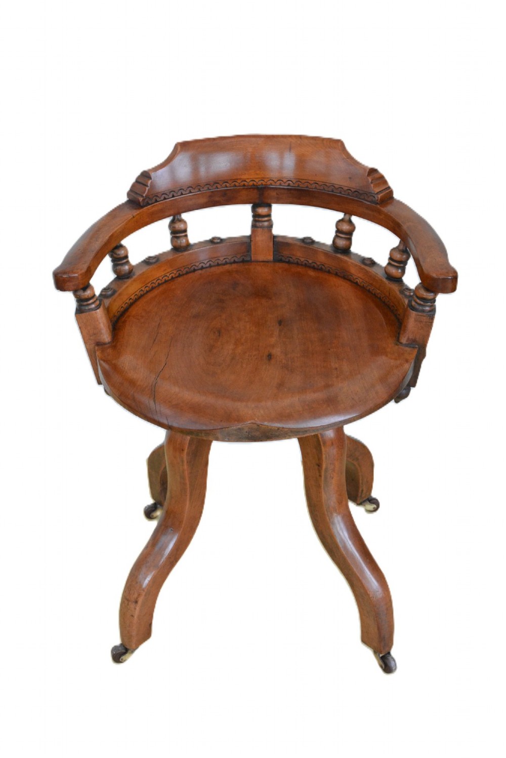 An antique walnut revolving desk chair featuring a curved horseshoe backrest with turned spindles, a circular wooden seat, and four splayed legs on castors.