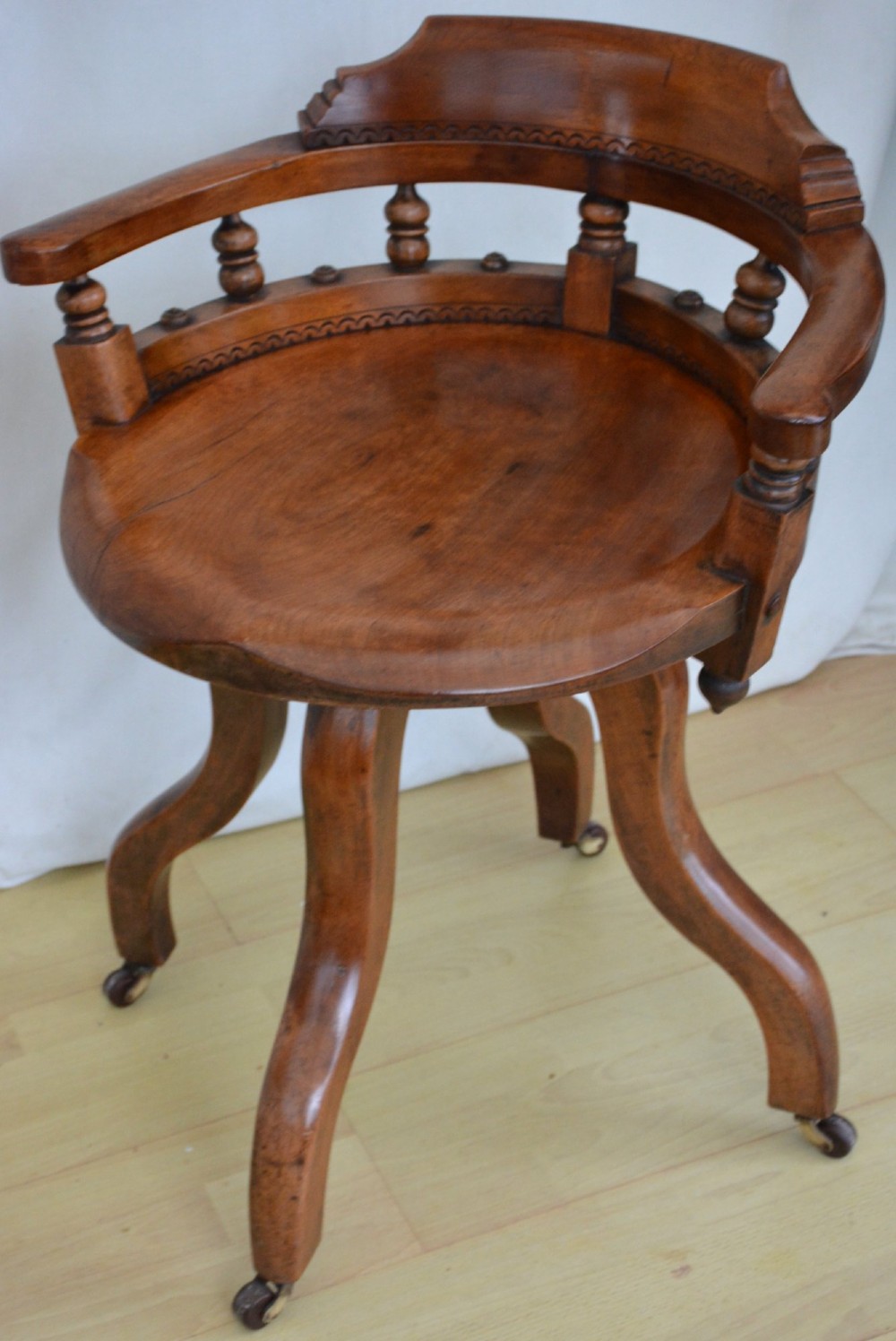 An antique walnut revolving desk chair featuring a curved horseshoe backrest with turned spindles, a circular wooden seat, and four splayed legs on castors. View II