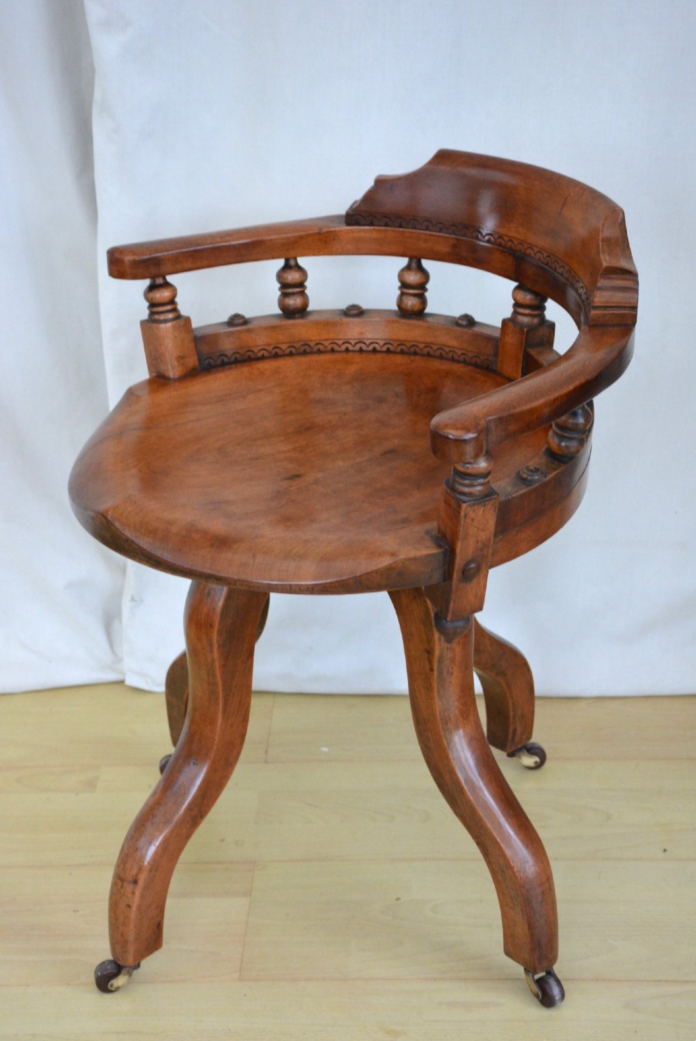 An antique walnut revolving desk chair featuring a curved horseshoe backrest with turned spindles, a circular wooden seat, and four splayed legs on castors. View III
