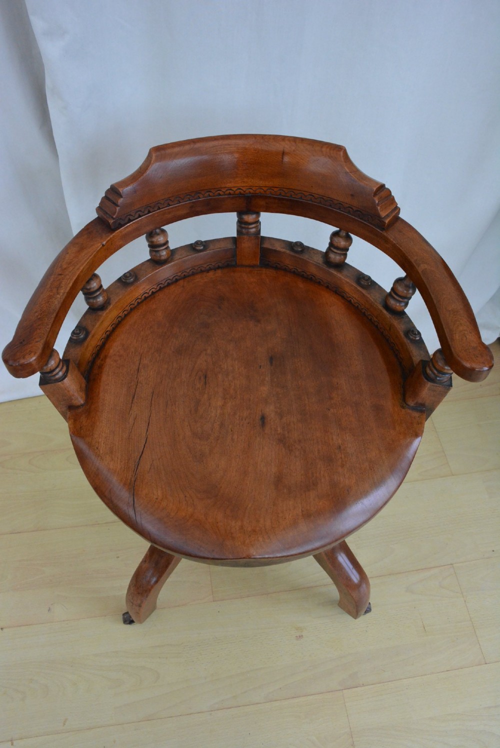An antique walnut revolving desk chair featuring a curved horseshoe backrest with turned spindles, a circular wooden seat, and four splayed legs on castors. View IV