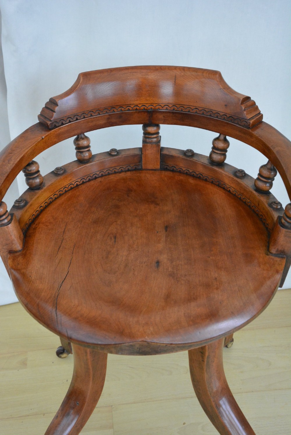 An antique walnut revolving desk chair featuring a curved horseshoe backrest with turned spindles, a circular wooden seat, and four splayed legs on castors. View V