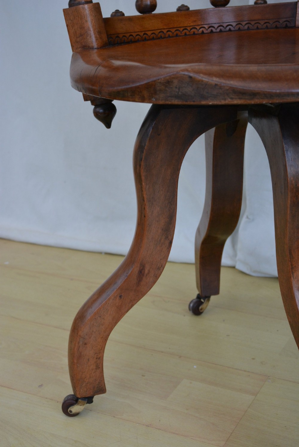 An antique walnut revolving desk chair featuring a curved horseshoe backrest with turned spindles, a circular wooden seat, and four splayed legs on castors. View VI