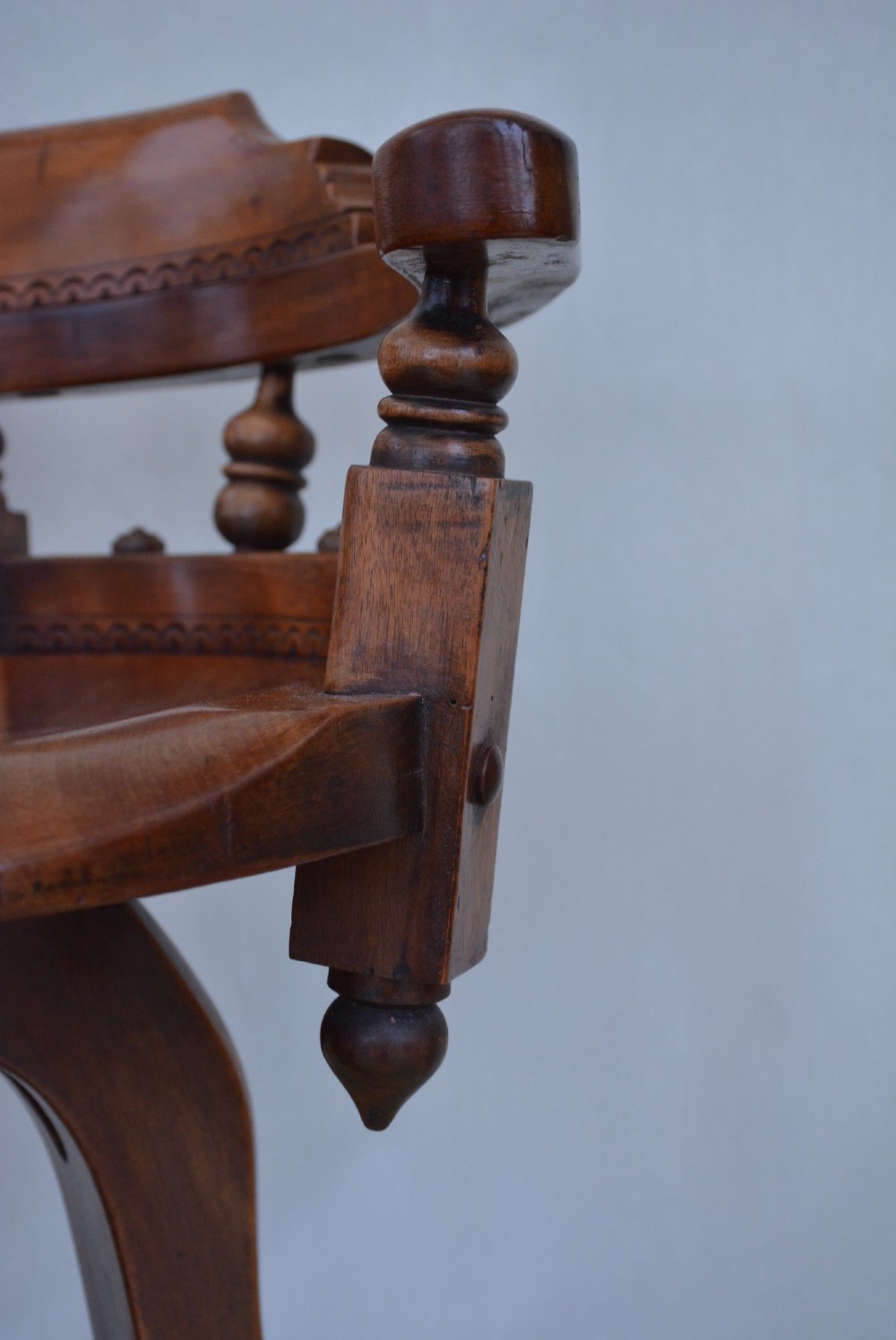 An antique walnut revolving desk chair featuring a curved horseshoe backrest with turned spindles, a circular wooden seat, and four splayed legs on castors. View X