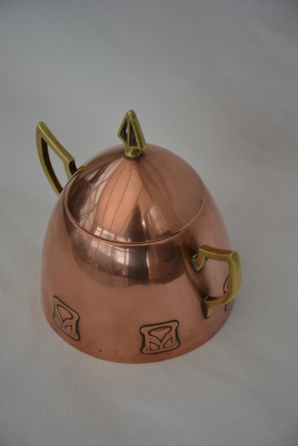An Art Nouveau copper sugar bowl featuring angular brass handles, a conical lid with a stylised finial, and embossed geometric motifs around the base. View III