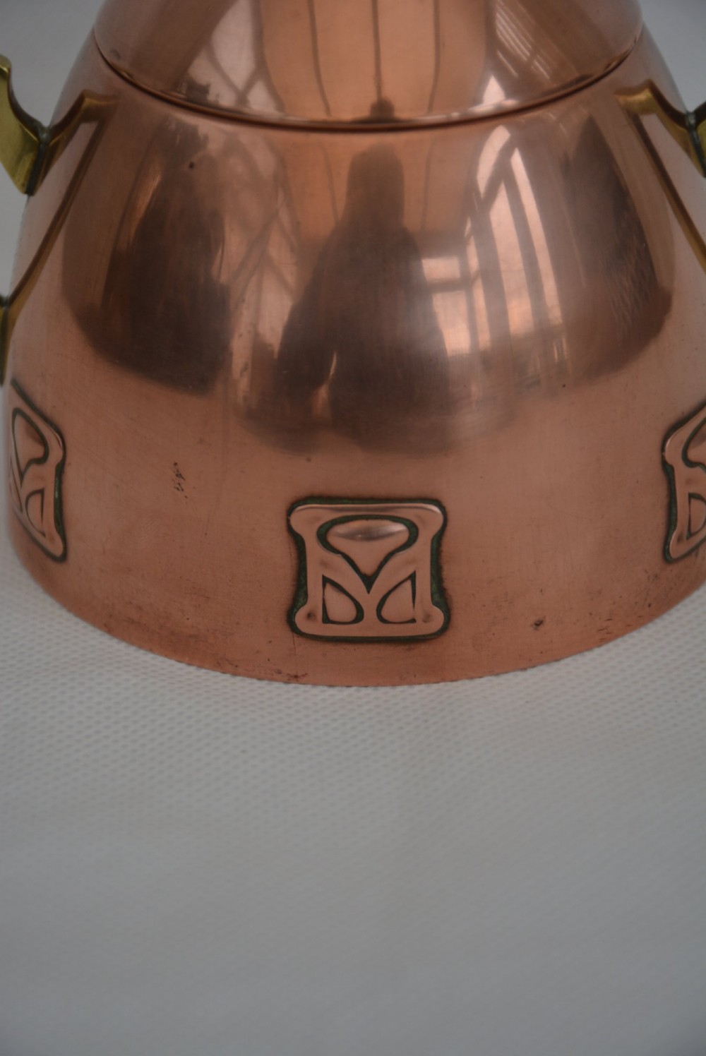 An Art Nouveau copper sugar bowl featuring angular brass handles, a conical lid with a stylised finial, and embossed geometric motifs around the base. View XV