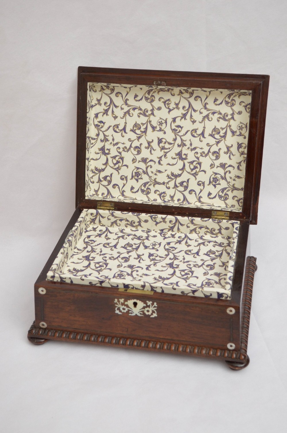 An open dark wood sarcophagus-shaped jewellery box featuring a mother-of-pearl escutcheon and a removable tray lined with floral paper. View III