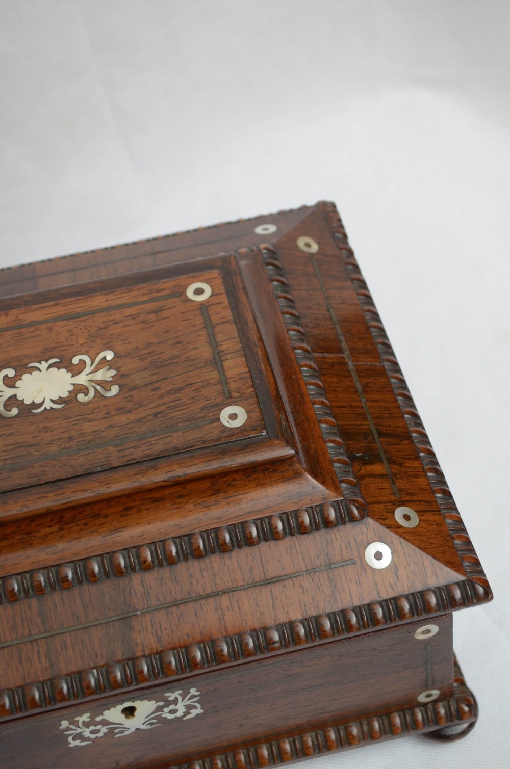 An open dark wood sarcophagus-shaped jewellery box featuring a mother-of-pearl escutcheon and a removable tray lined with floral paper. View X