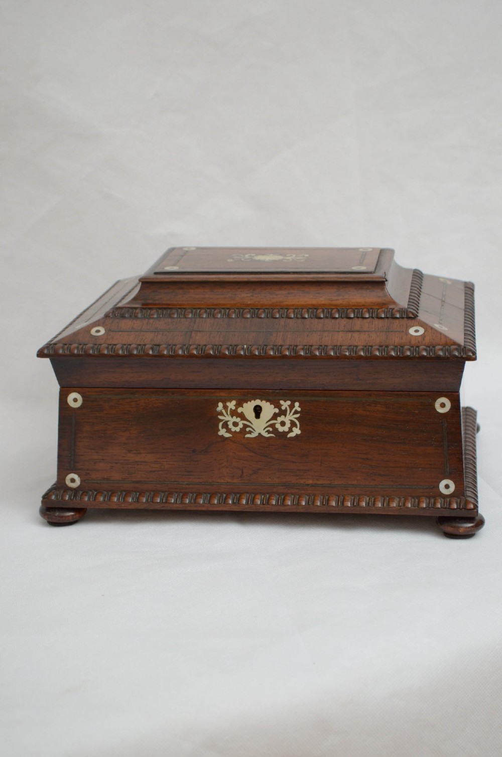 An open dark wood sarcophagus-shaped jewellery box featuring a mother-of-pearl escutcheon and a removable tray lined with floral paper. View XI