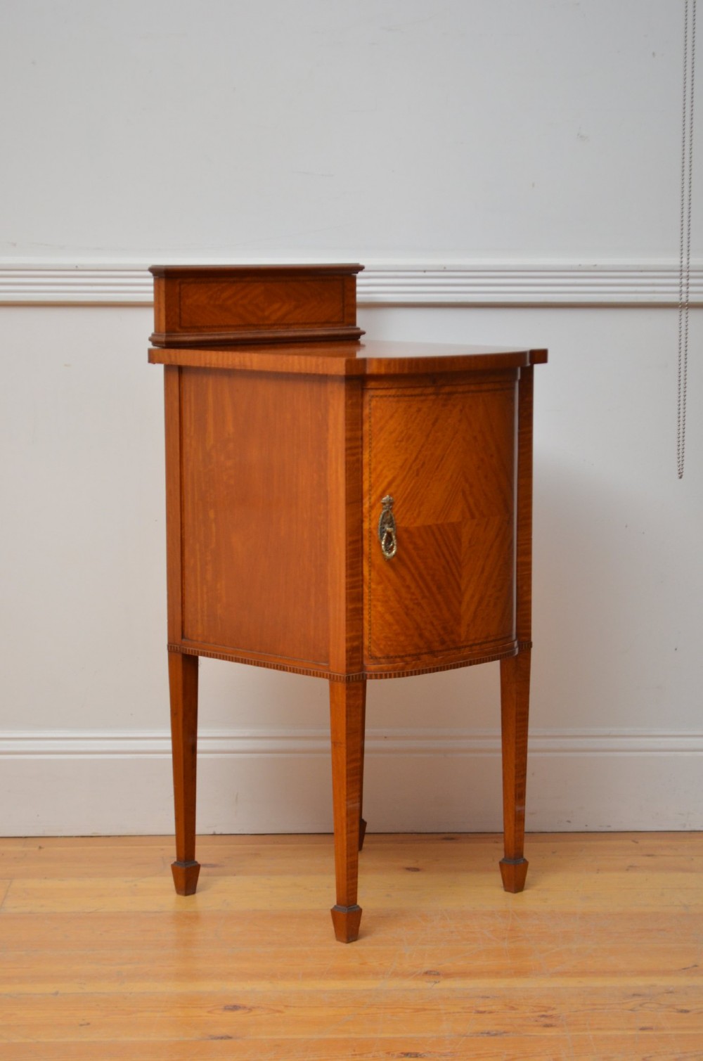 An Edwardian satinwood bedside cabinet with a gallery upstand top, diamond-patterned veneered cupboard door, and square tapered legs. View V