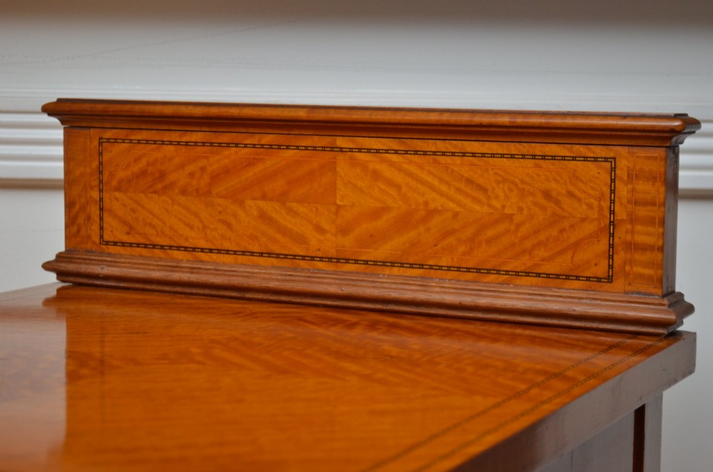 An Edwardian satinwood bedside cabinet with a gallery upstand top, diamond-patterned veneered cupboard door, and square tapered legs. View VI