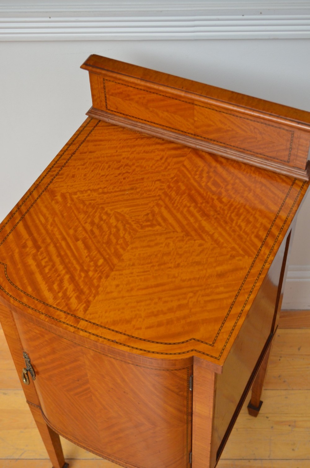 An Edwardian satinwood bedside cabinet with a gallery upstand top, diamond-patterned veneered cupboard door, and square tapered legs. View VII