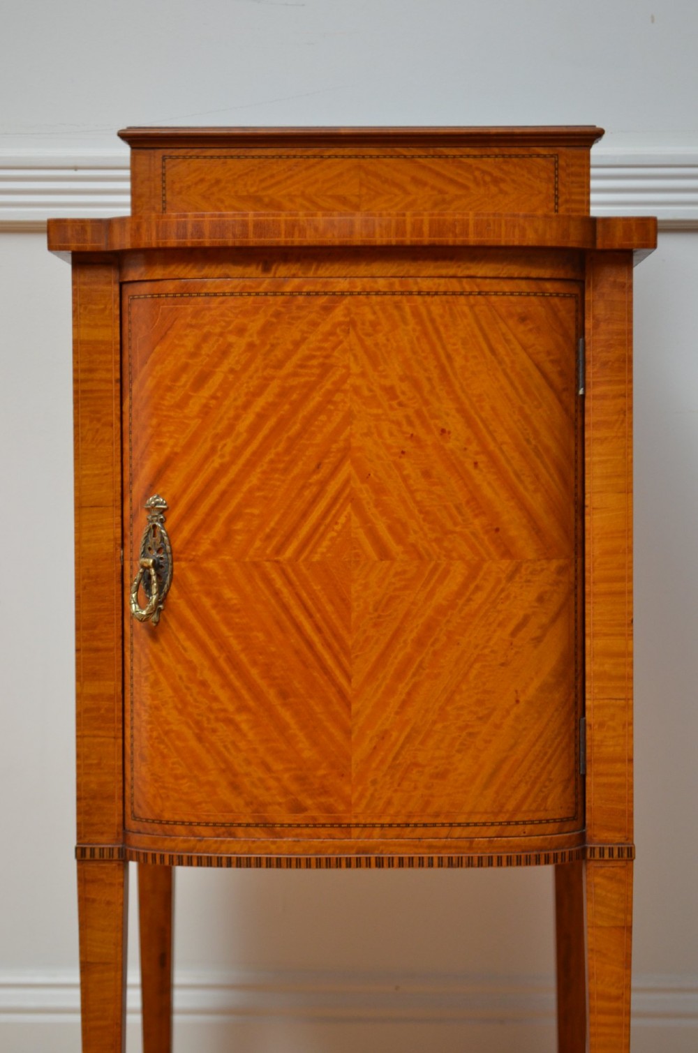 An Edwardian satinwood bedside cabinet with a gallery upstand top, diamond-patterned veneered cupboard door, and square tapered legs. View IX