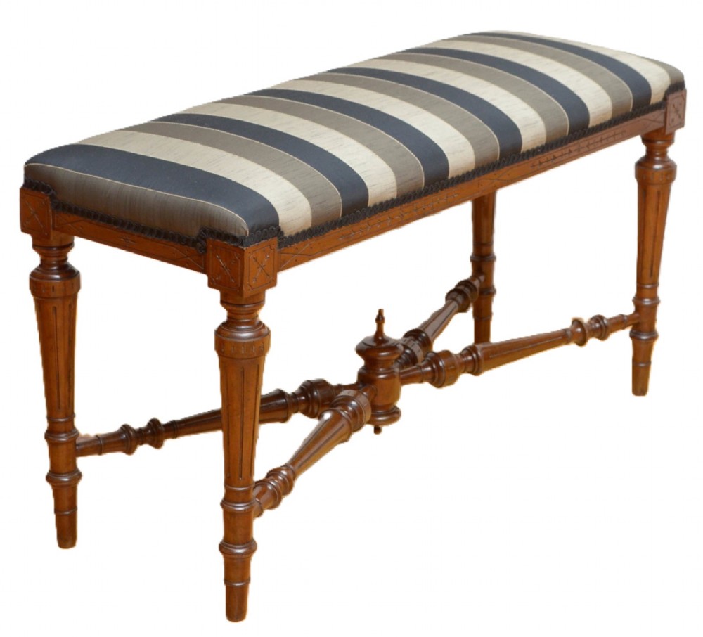 A Victorian walnut window seat featuring a striped upholstered top, fluted turned legs, and an intricate cross-stretcher with a central finial.