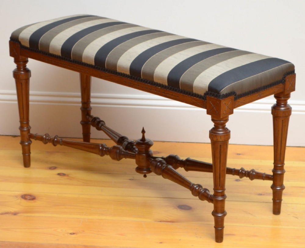 A Victorian walnut window seat featuring a striped upholstered top, fluted turned legs, and an intricate cross-stretcher with a central finial. View IV