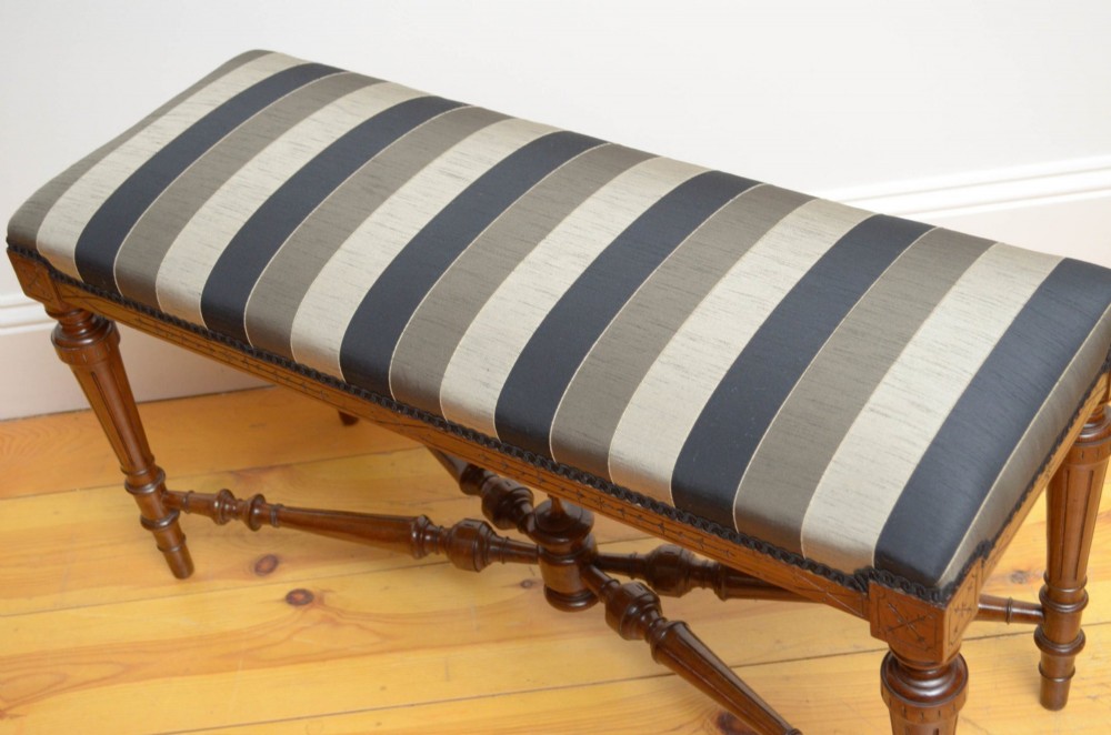 A Victorian walnut window seat featuring a striped upholstered top, fluted turned legs, and an intricate cross-stretcher with a central finial. View VII