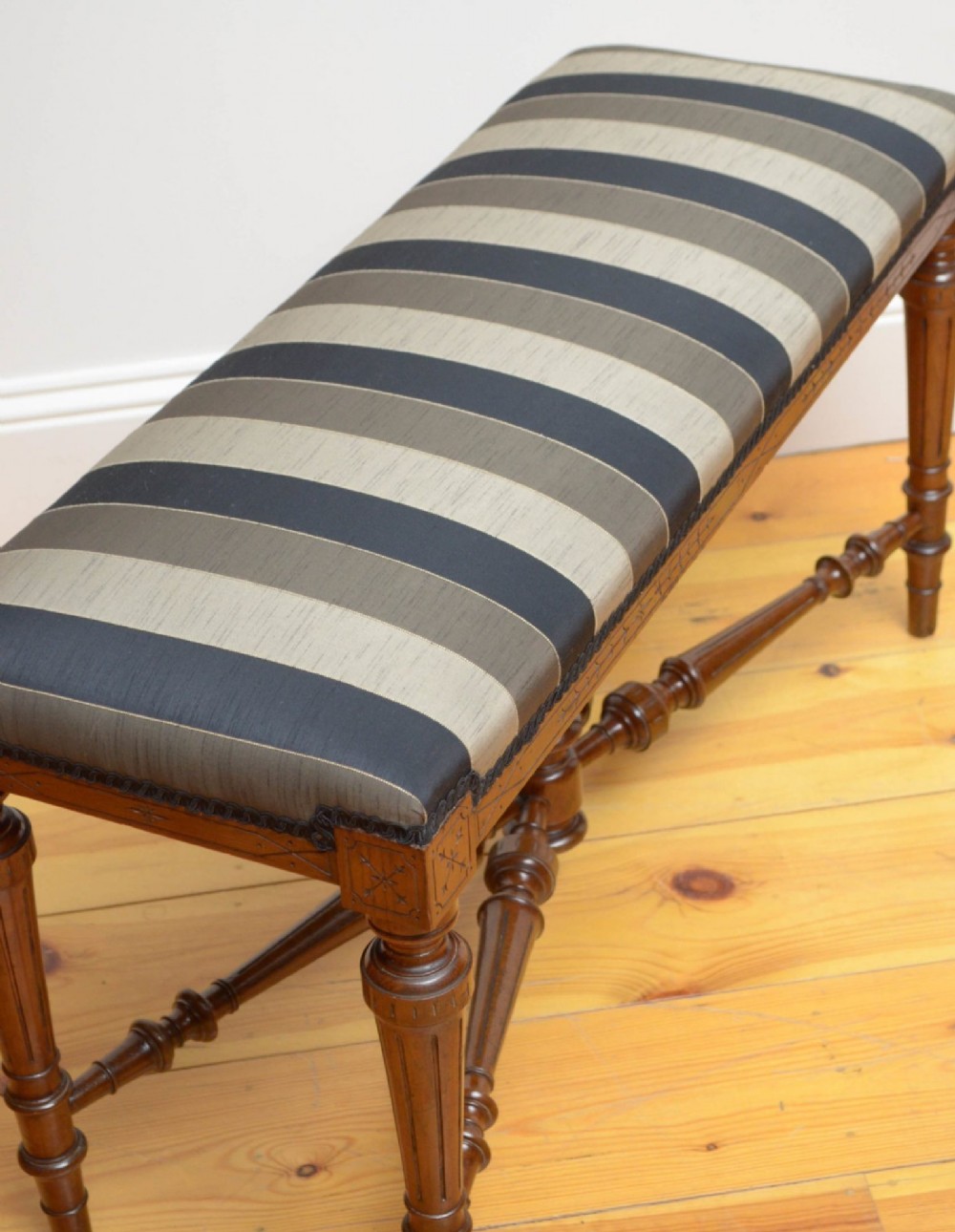 A Victorian walnut window seat featuring a striped upholstered top, fluted turned legs, and an intricate cross-stretcher with a central finial. View VIII