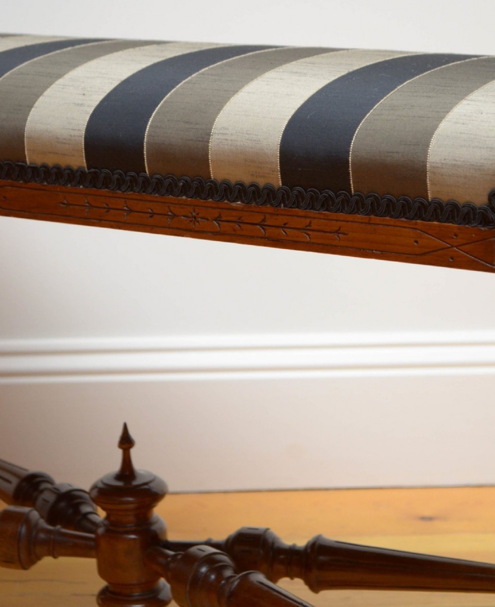 A Victorian walnut window seat featuring a striped upholstered top, fluted turned legs, and an intricate cross-stretcher with a central finial. View IX