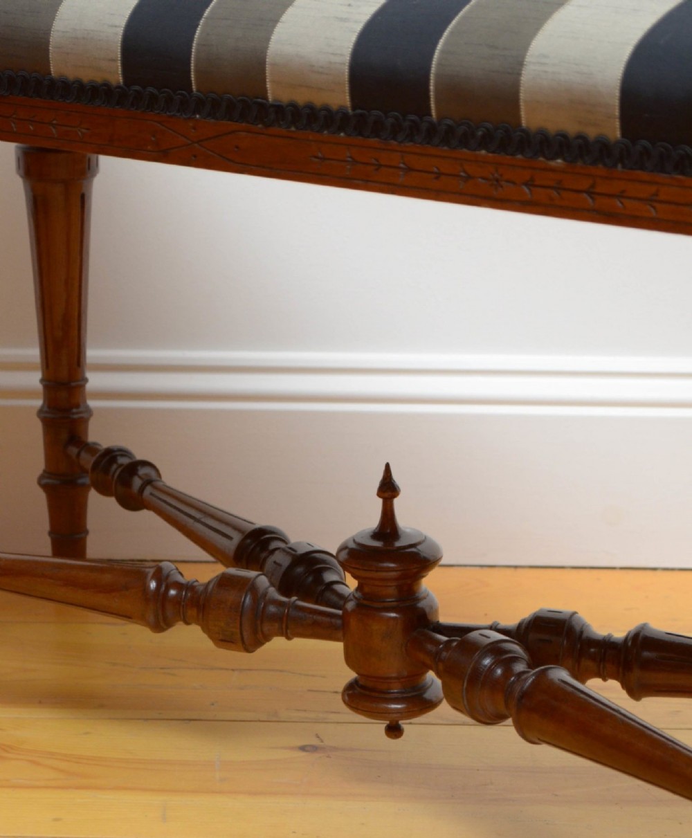 A Victorian walnut window seat featuring a striped upholstered top, fluted turned legs, and an intricate cross-stretcher with a central finial. View XI