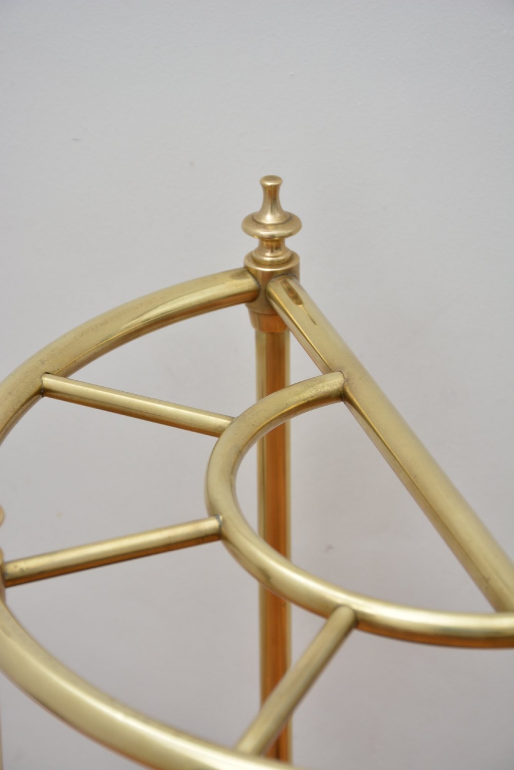 A semi-circular brass umbrella stand featuring finial tops, vertical tubular legs, a partitioned top frame, and a black drip tray base. View VII