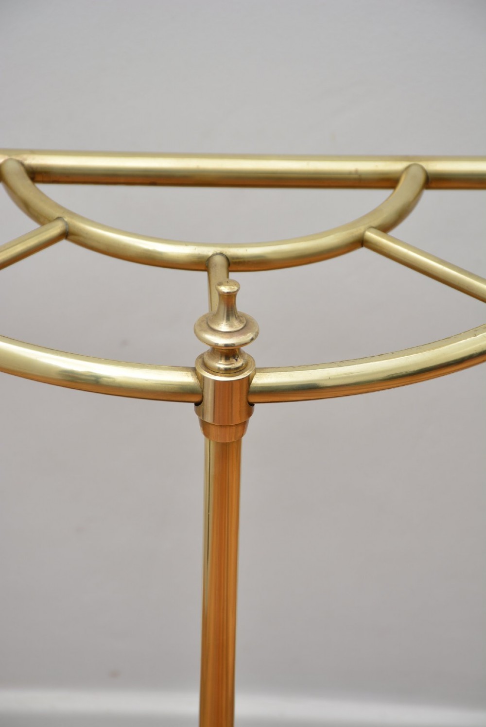 A semi-circular brass umbrella stand featuring finial tops, vertical tubular legs, a partitioned top frame, and a black drip tray base. View VIII