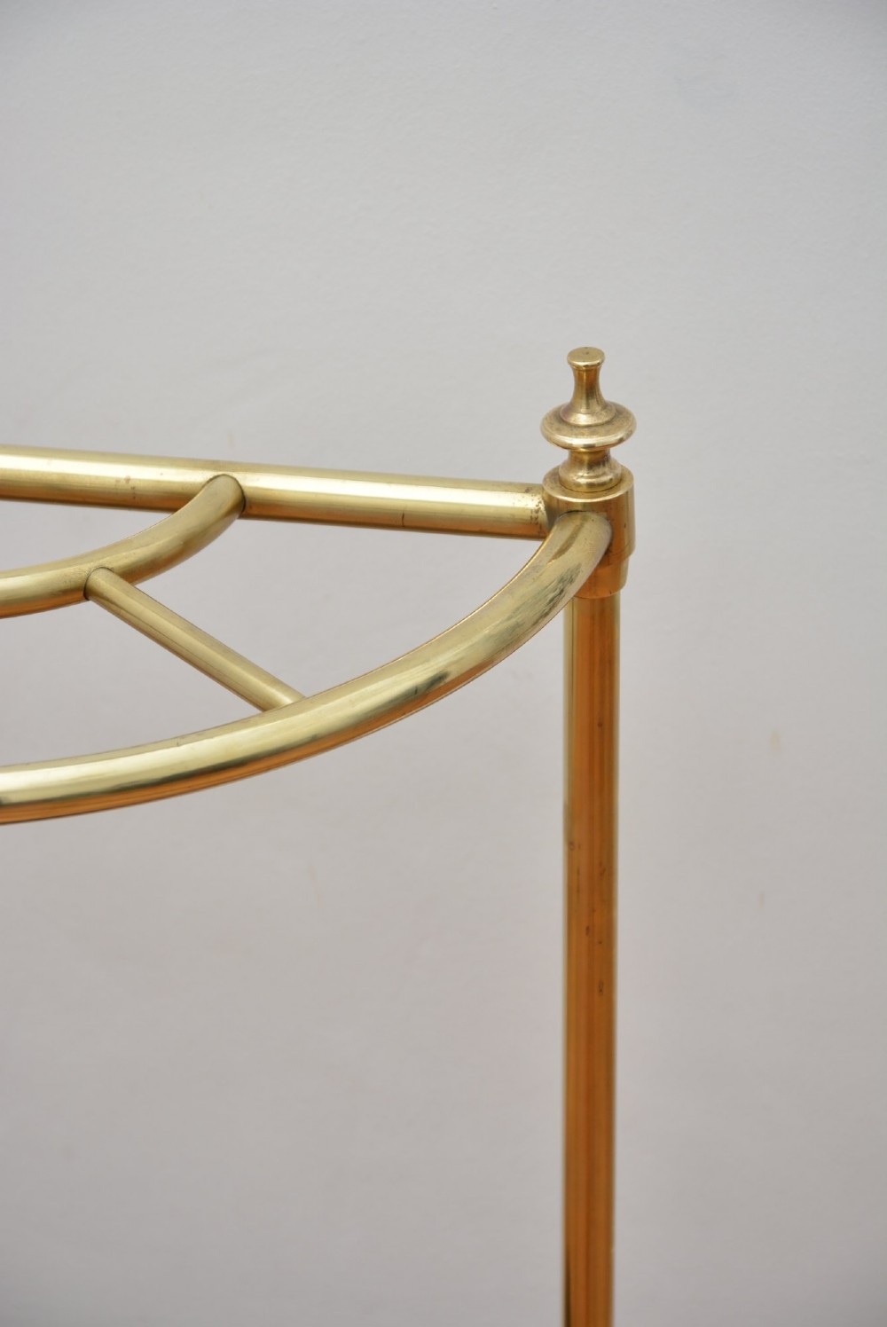 A semi-circular brass umbrella stand featuring finial tops, vertical tubular legs, a partitioned top frame, and a black drip tray base. View IX