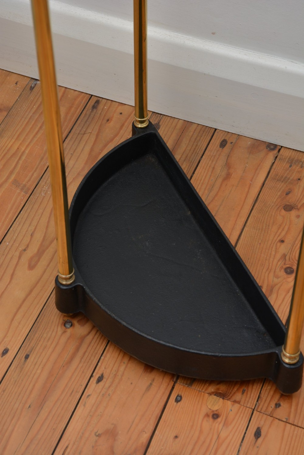 A semi-circular brass umbrella stand featuring finial tops, vertical tubular legs, a partitioned top frame, and a black drip tray base. View XI