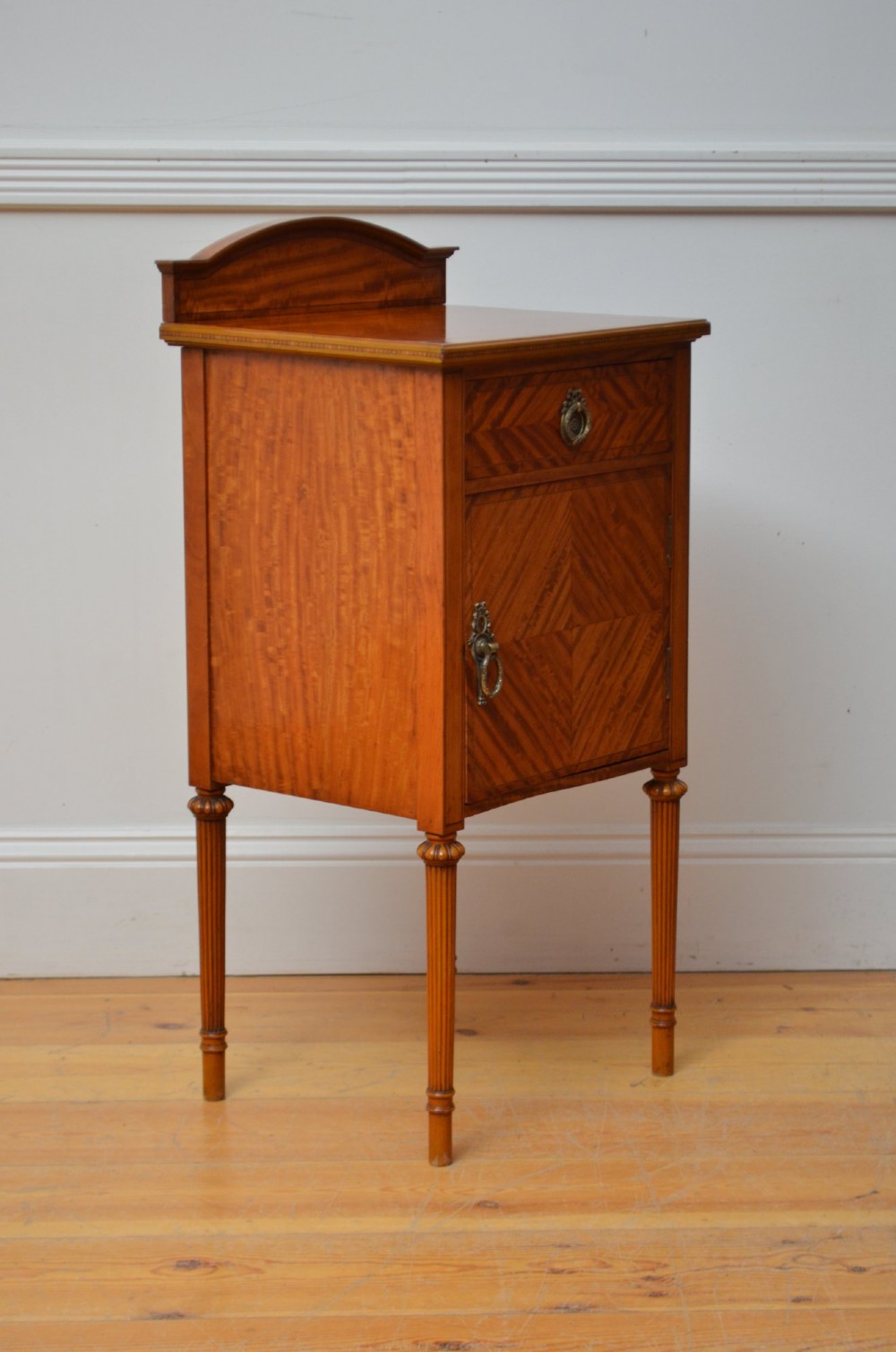 An Edwardian satinwood bedside cupboard featuring chevron veneer detailing, an upper drawer, a lower door, and turned reeded legs. View II