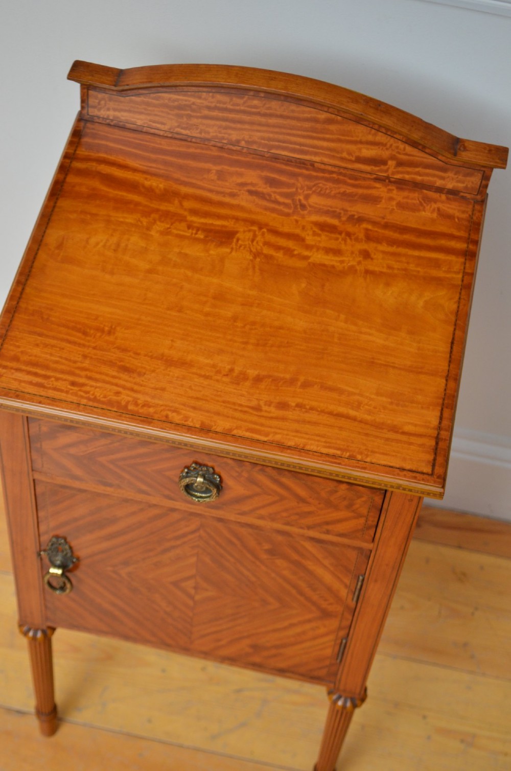An Edwardian satinwood bedside cupboard featuring chevron veneer detailing, an upper drawer, a lower door, and turned reeded legs. View IV