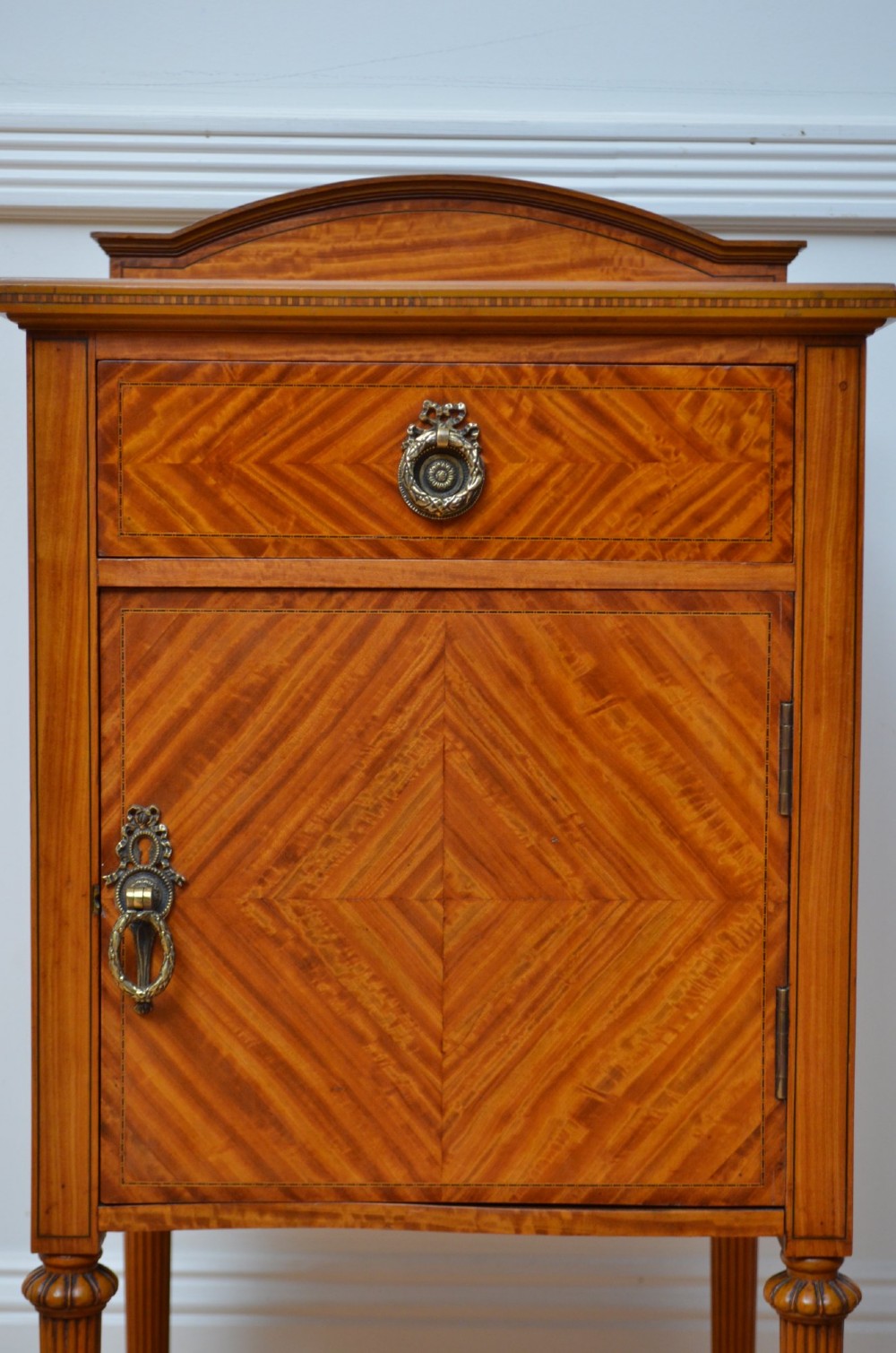 An Edwardian satinwood bedside cupboard featuring chevron veneer detailing, an upper drawer, a lower door, and turned reeded legs. View VII