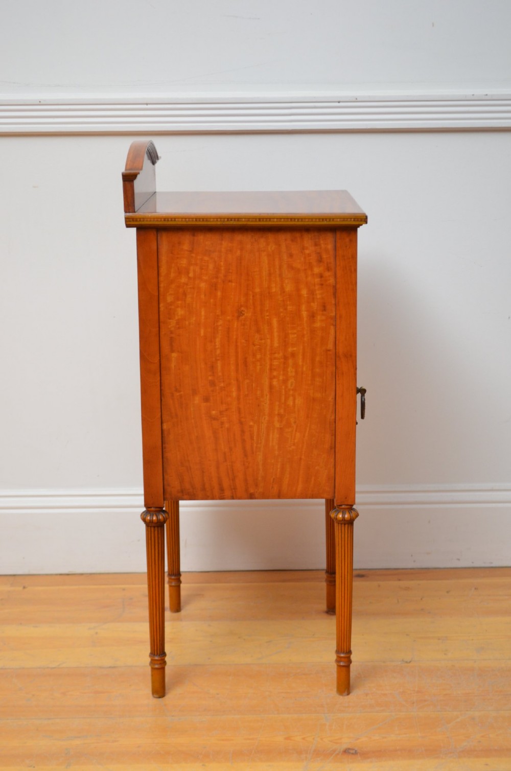 An Edwardian satinwood bedside cupboard featuring chevron veneer detailing, an upper drawer, a lower door, and turned reeded legs. View VIII