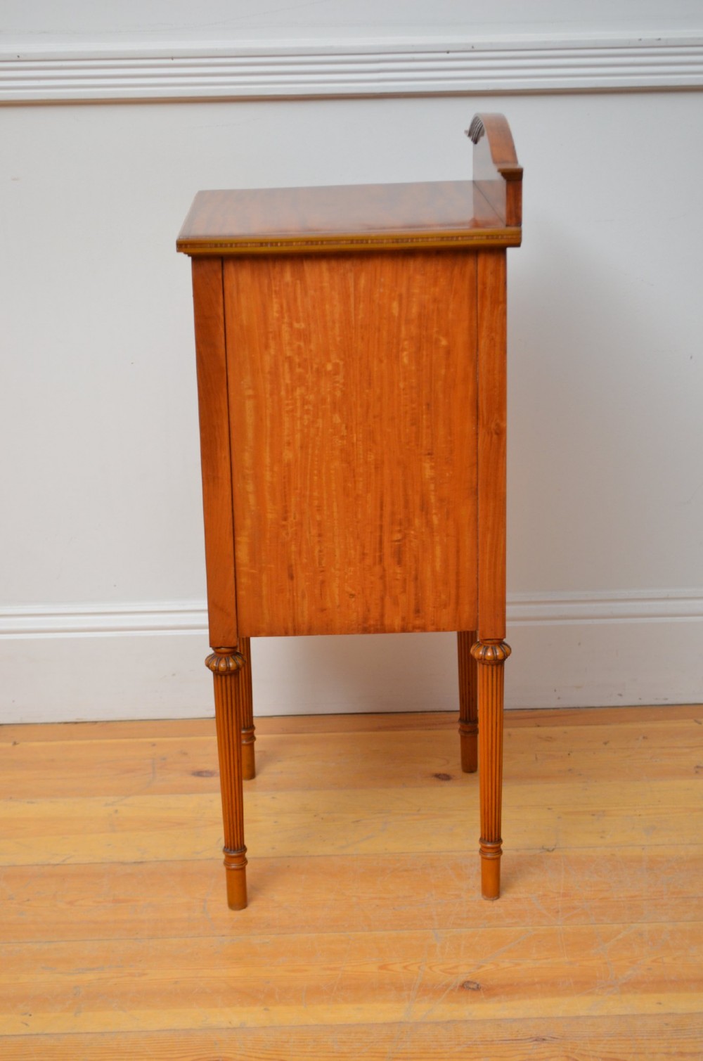 An Edwardian satinwood bedside cupboard featuring chevron veneer detailing, an upper drawer, a lower door, and turned reeded legs. View X