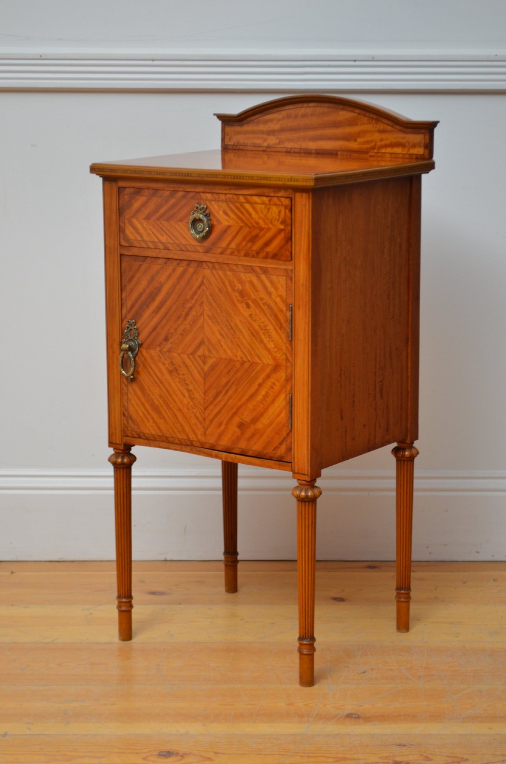 An Edwardian satinwood bedside cupboard featuring chevron veneer detailing, an upper drawer, a lower door, and turned reeded legs. View XI