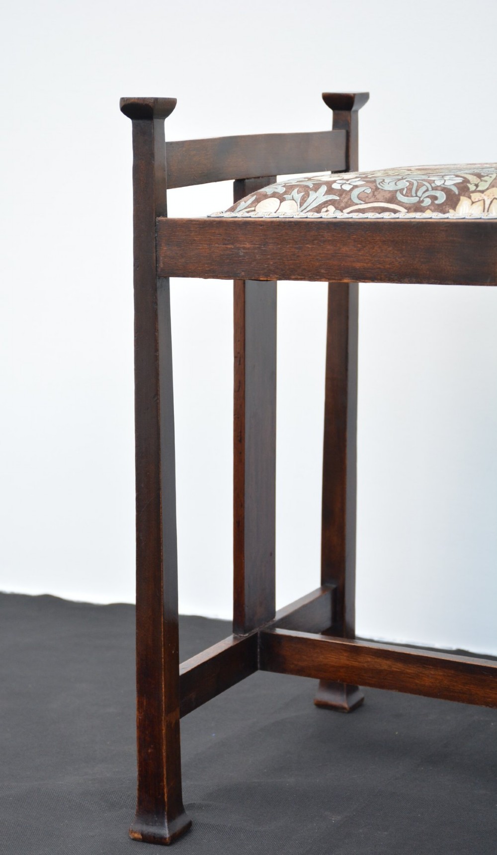 An antique dark mahogany Arts and Crafts stool featuring upright corner posts with square finials, vertical side splats, and a pattern-upholstered fabric seat. View IV