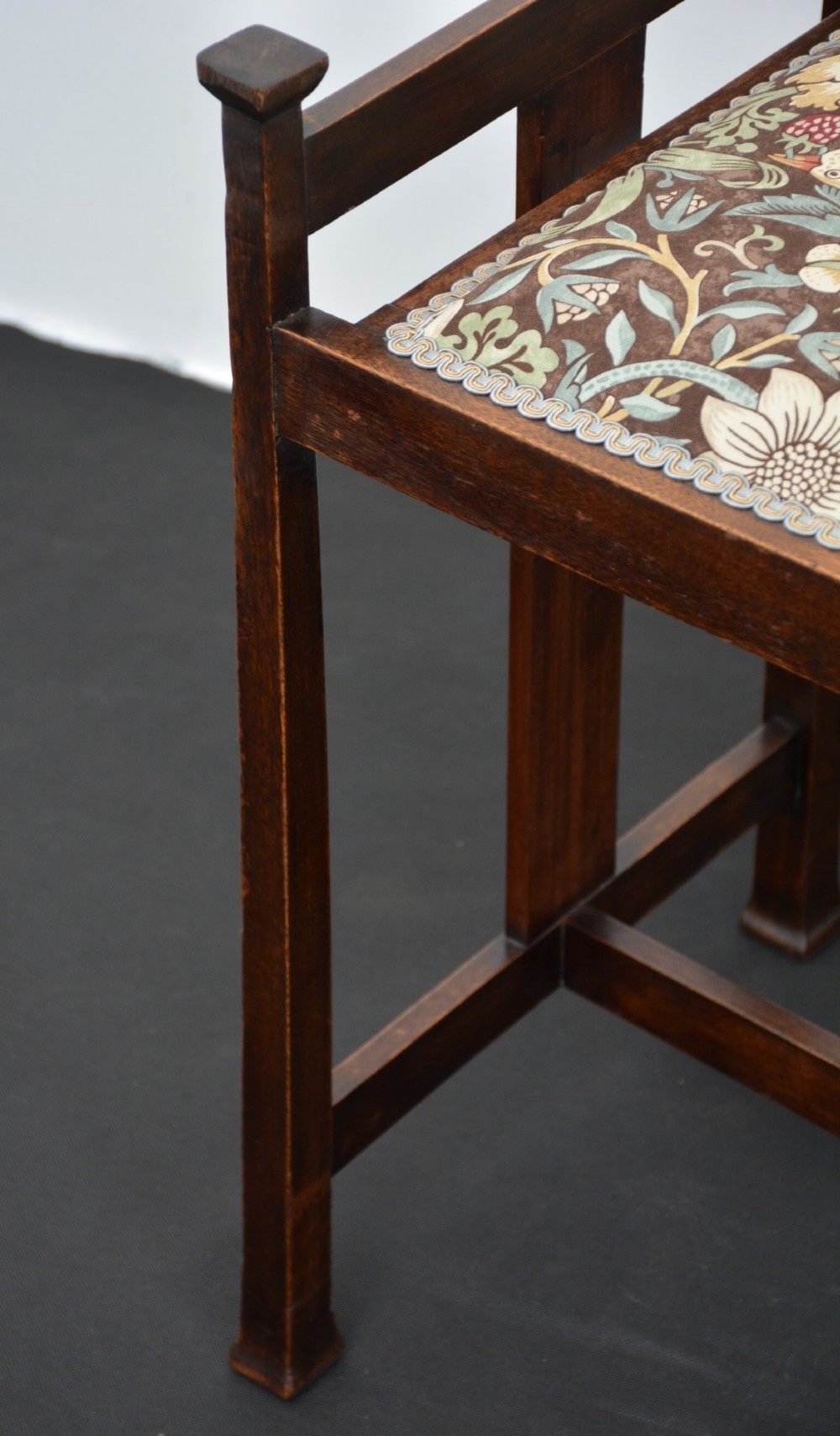 An antique dark mahogany Arts and Crafts stool featuring upright corner posts with square finials, vertical side splats, and a pattern-upholstered fabric seat. View VIII