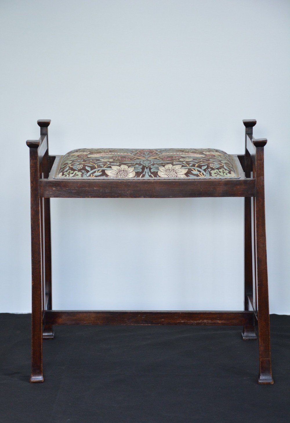An antique dark mahogany Arts and Crafts stool featuring upright corner posts with square finials, vertical side splats, and a pattern-upholstered fabric seat. View XIII