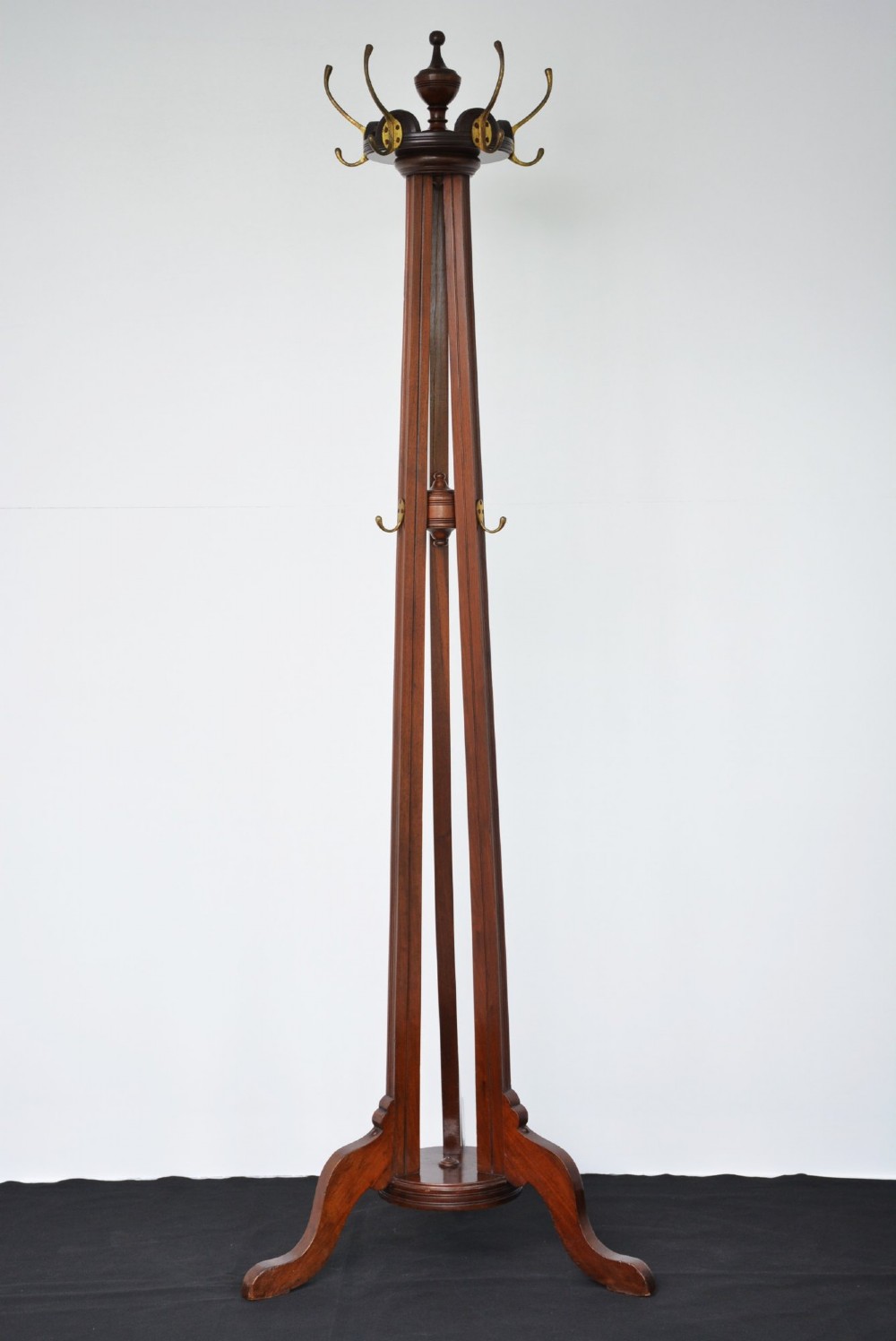 A tall freestanding dark walnut coat stand featuring a slatted central column, brass hooks, a turned finial, and four splayed feet.