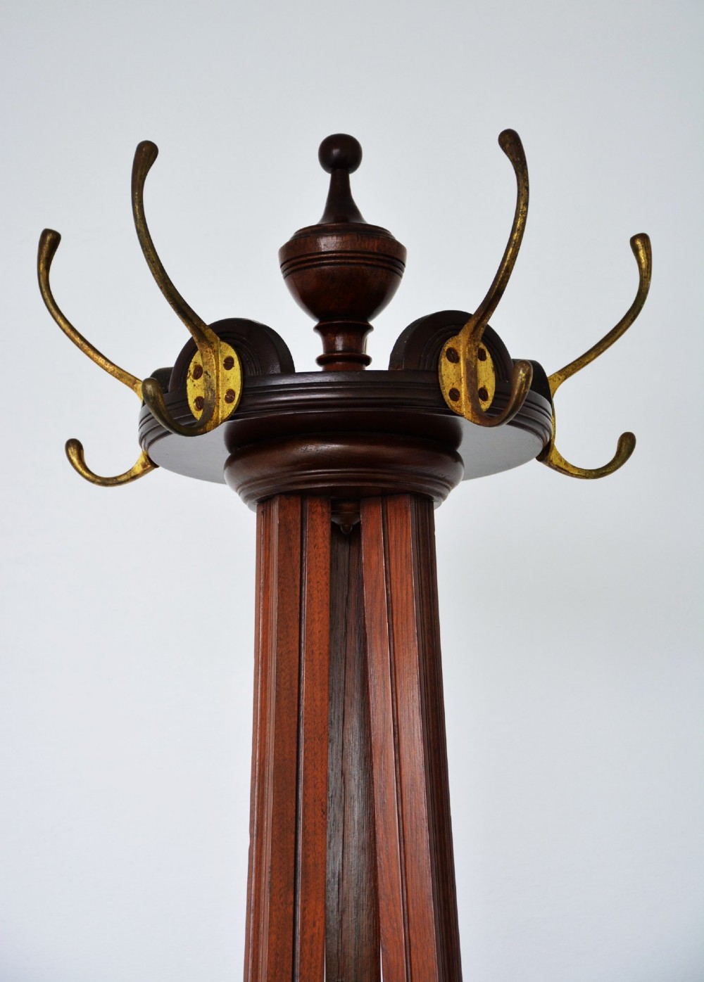 A tall freestanding dark walnut coat stand featuring a slatted central column, brass hooks, a turned finial, and four splayed feet. View VII
