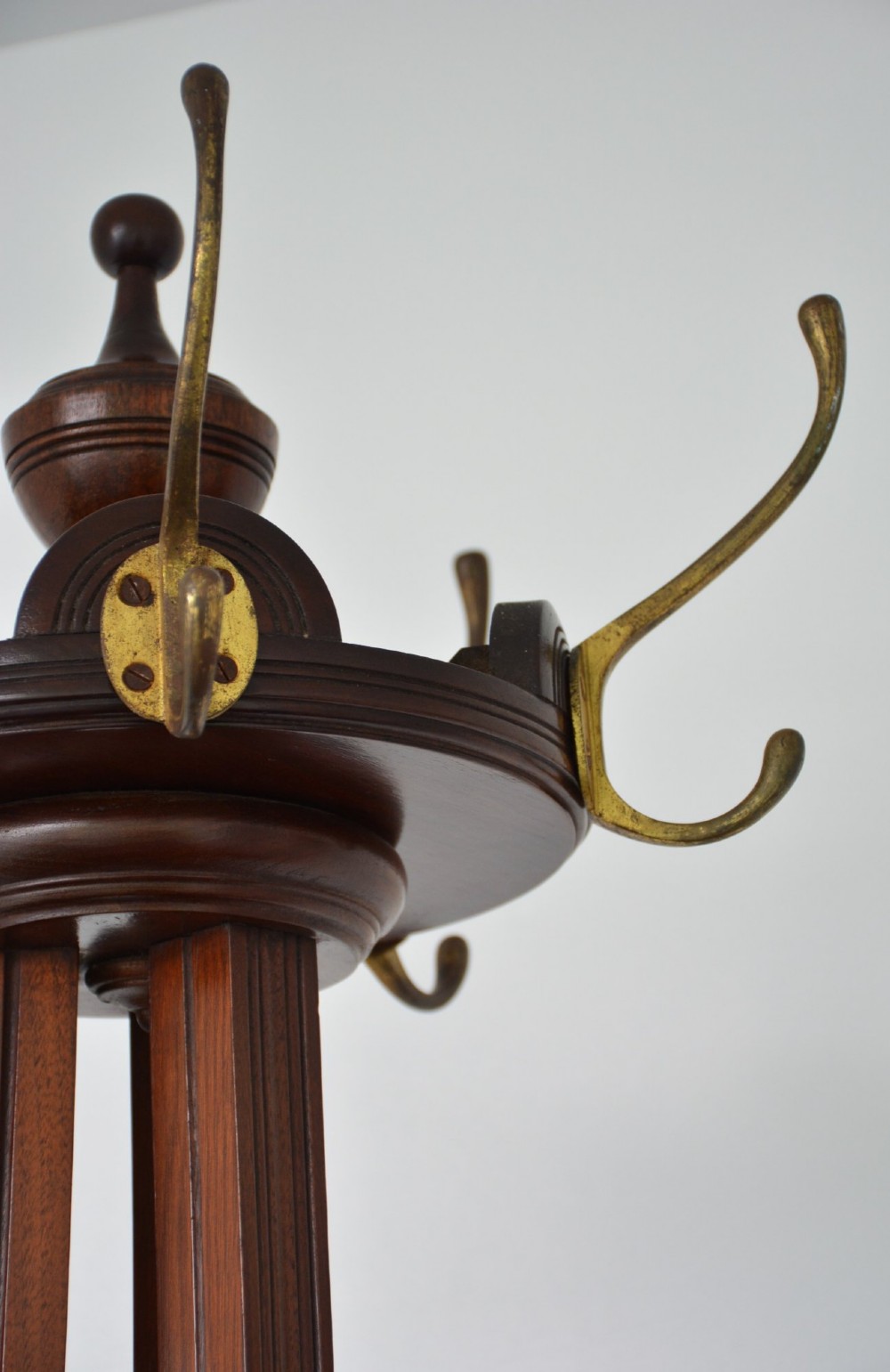 A tall freestanding dark walnut coat stand featuring a slatted central column, brass hooks, a turned finial, and four splayed feet. View VIII