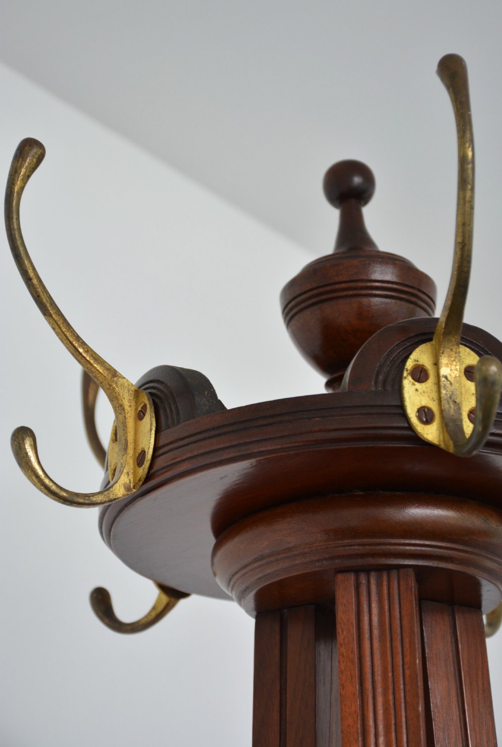 A tall freestanding dark walnut coat stand featuring a slatted central column, brass hooks, a turned finial, and four splayed feet. View IX